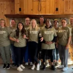 12-women-smiling-in-front-of-a-cabin-fireplace-at-their-warriors-ascent-graduation-in-fall-2025