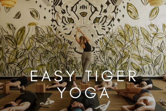 A yoga instructor leads a group class beneath a mural featuring a tiger, representing Easy Tiger Yoga.